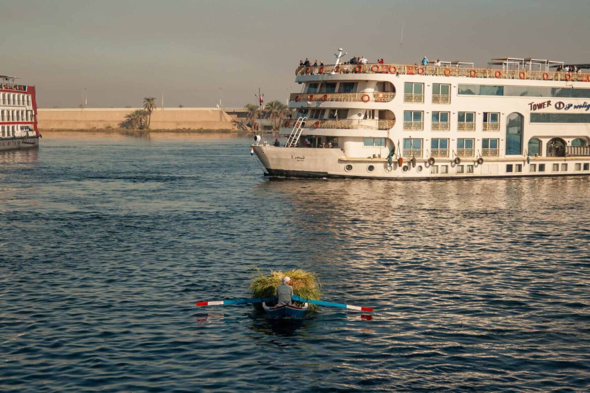 Barco tipo crucero del Nilo (Egipto) entrando a un puerto con una barca de recolector de hierba del Río agua con reflejo