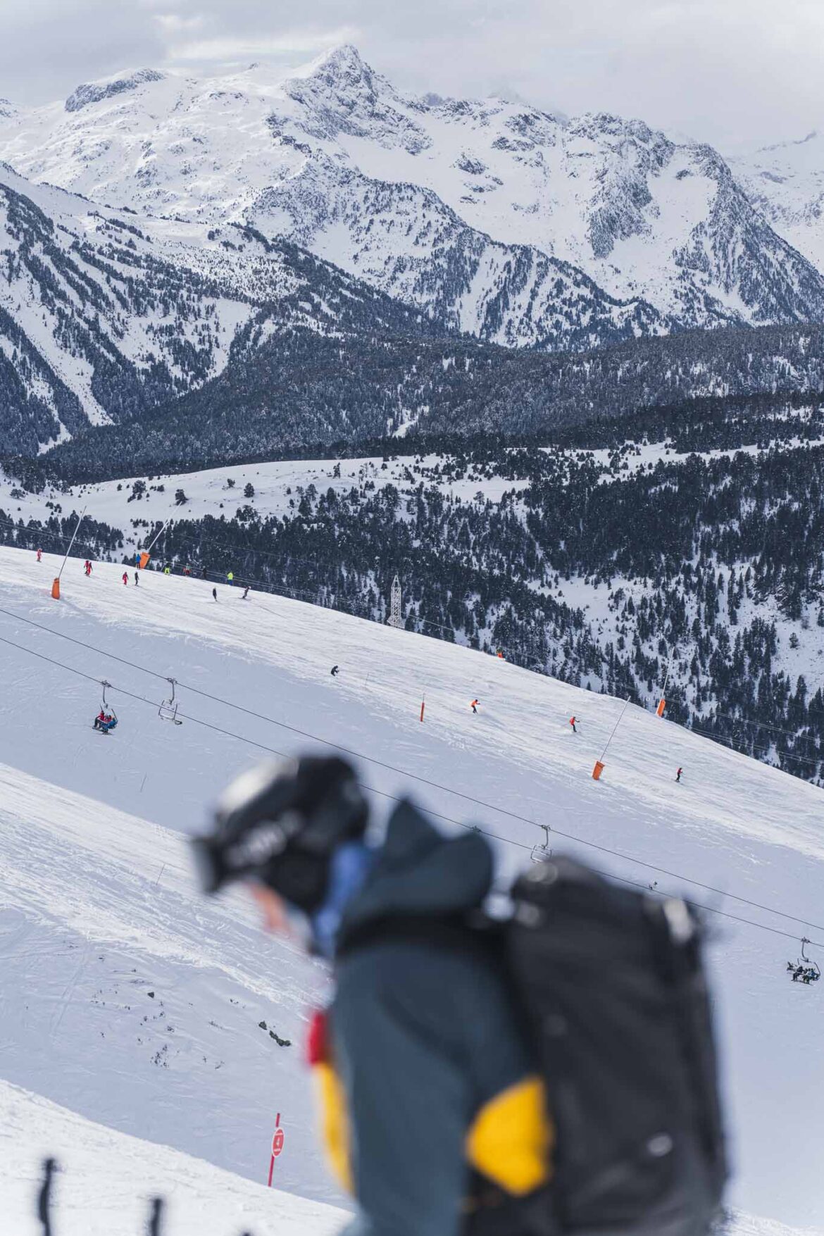 La cima de la montaña del Montardo al fondo, las pistas de Baqueira Beret en segundo plano y la silueta de una persona con casco y una mochila posiblemente para transportar un equipo de fotografía o video